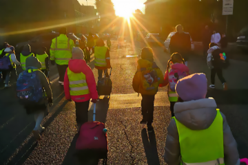 Bambine e bambini camminano in strada con zaini e pettorine colorate