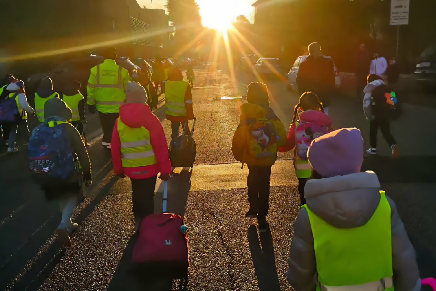 Bambine e bambini camminano in strada con zaini e pettorine colorate