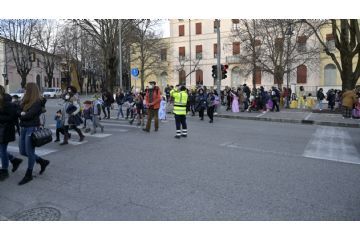 Bambini e genitori che attraversano la strada con l'aiuto della polizia locale, in secondo piano la scuola.