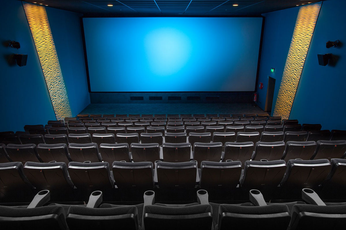 sala cinematografica con schermo illuminato e poltrone in primo piano