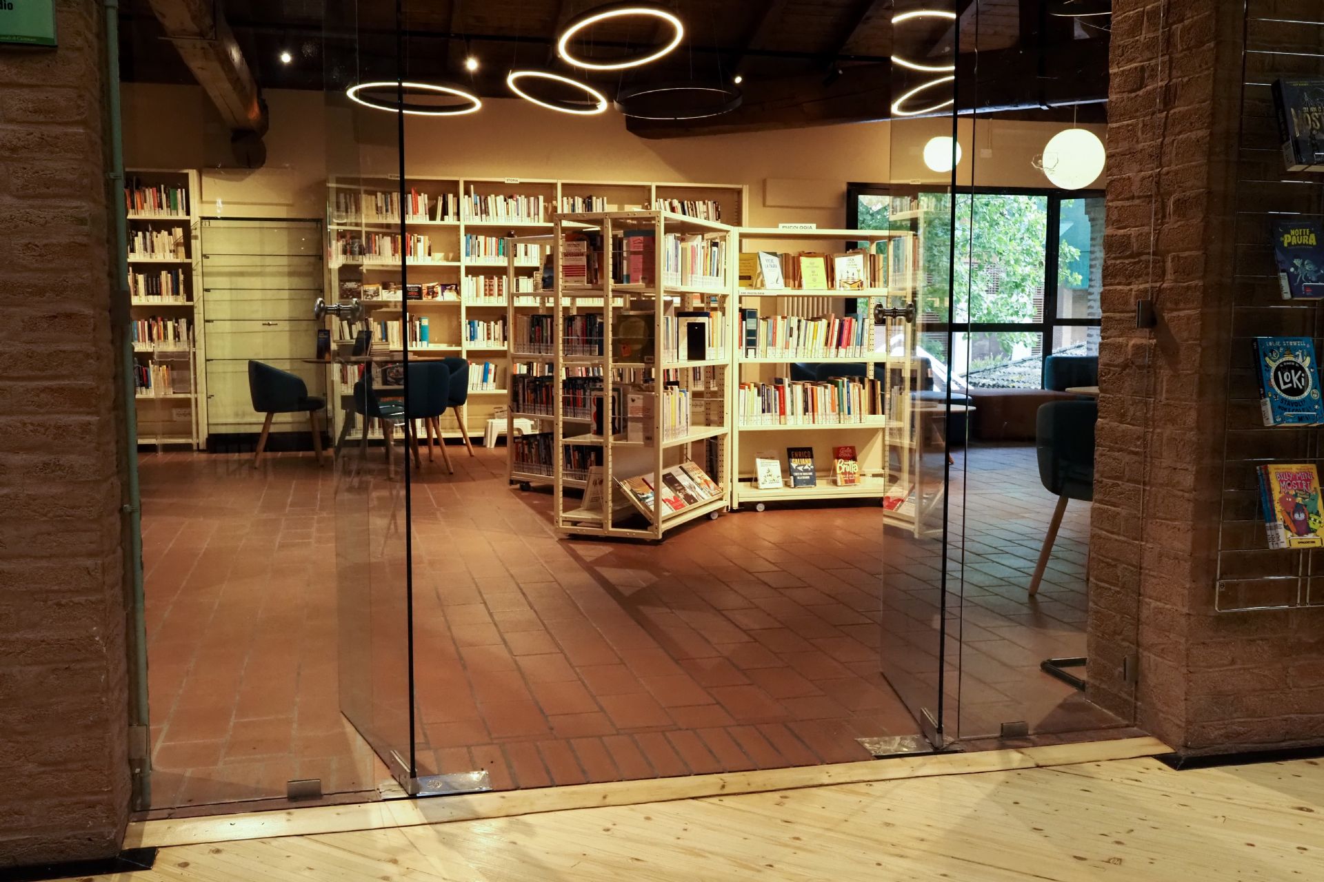 una sezione della biblioteca con scansie di libri, luci circolari e porta d'ingresso