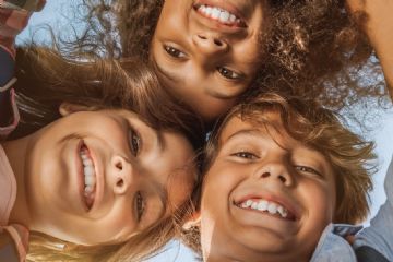 Bambine e bambiini sorridenti in primo piano fotografati dal basso.